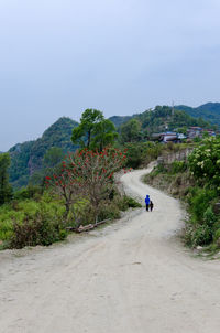 Children walking on dirt road on mountains against sky