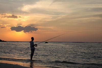 Silhouette man fishing in sea against sunset sky