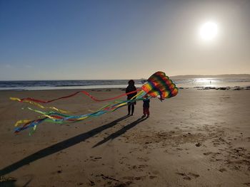 Rear view of mother and daughter with kite standing on beach against sky