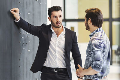 Young businessman pinning paper on notice board while talking with colleague in office