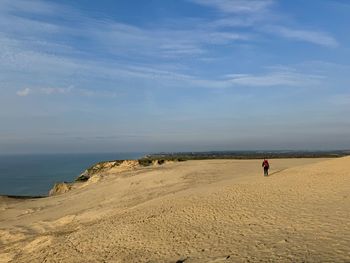 Rear view of man walking on beach against sky