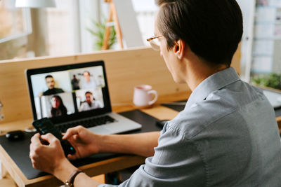 Side view of smiling male manager having video conference online via laptop while sitting at table and working from home during coronavirus epidemic