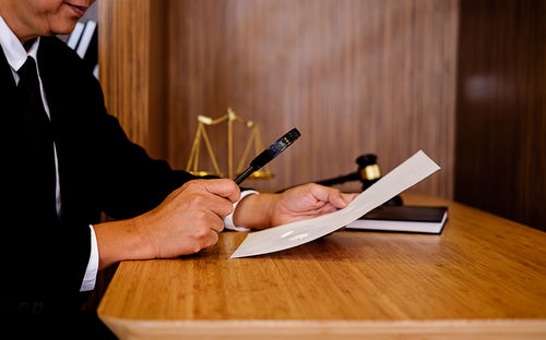 Midsection of male lawyer analyzing document while sitting in office