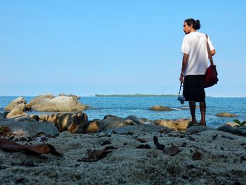 Rear view of man standing at beach against clear sky