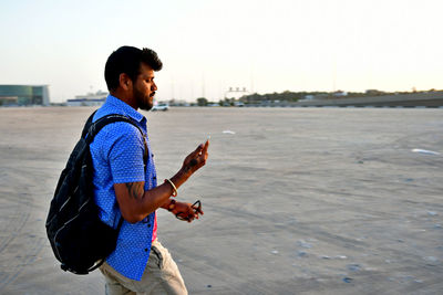 Side view of young man holding mobile phone while walking in city