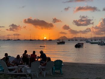 People sitting on beach against sky during sunset