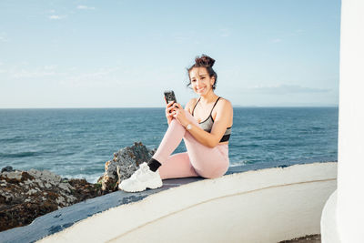 Portrait of young woman sitting on sea against sky