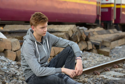 Young man looking down while sitting on railroad track