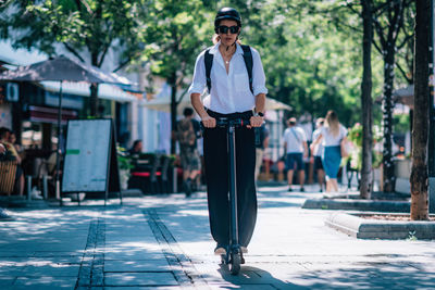 Full length of woman riding electric push scooter on walkway