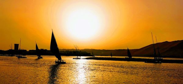 Silhouette sailboats in sea against orange sky