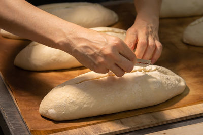 Close-up of a baker's female hands cutting a loaf of dough into a loaf of bread with a blade before