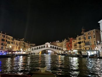 Bridge over river by illuminated buildings in city at night