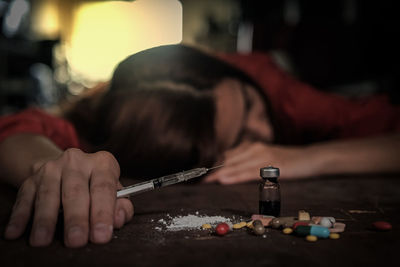 Woman holding syringe by pills and bottle on table