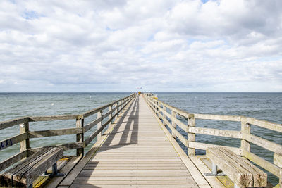 A wooden footbridge leads across the moving sea to the horizon under a thickly clouded sky