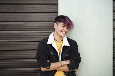 Portrait of smiling young woman standing against wall