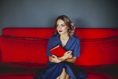 Beautiful young woman holding book sitting on sofa
