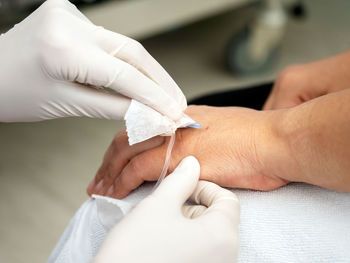 Cropped image of doctor removing medical equipment from patient hand in hospital