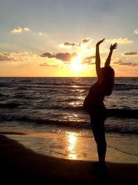 Pregnant woman practicing yoga at beach against sky during sunset