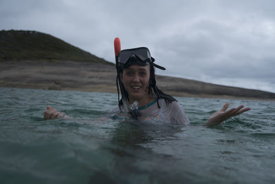 Portrait of smiling young woman snorkeling in sea against cloudy sky