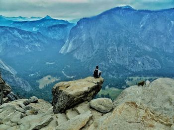 Rear view of man sitting on rock against mountains