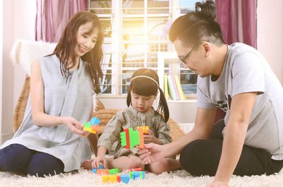 Parents playing with daughter on carpet at home 