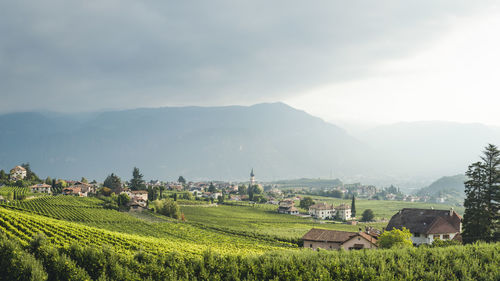 Scenic view of agricultural field by houses and mountains against sky