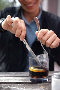 Midsection of woman putting ice cube in drink on table