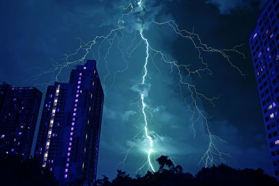 Low angle view of lightning over illuminated buildings at night