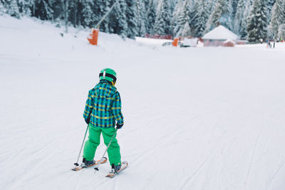 Rear view of boy skiing on snow covered land
