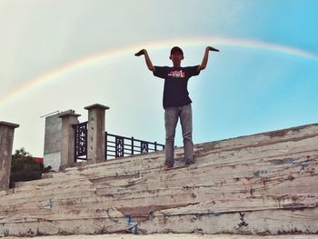 Optical illusion of man carrying rainbow while standing on steps