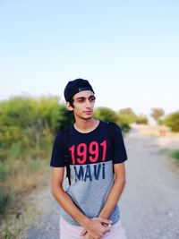 Man wearing cap looking away while standing on dirt road