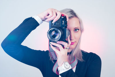 Portrait of smiling woman holding camera against white background