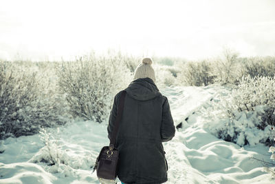 Rear view of woman walking on snow covered field