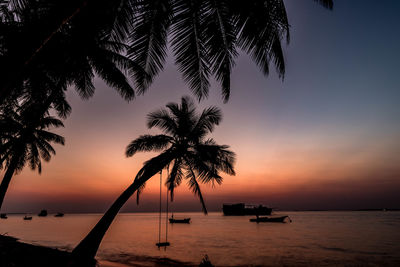 Silhouette palm trees by sea against sky during sunset