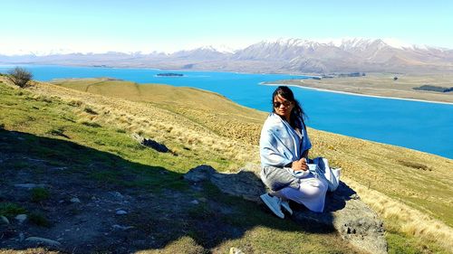 Woman sitting by lake on hill