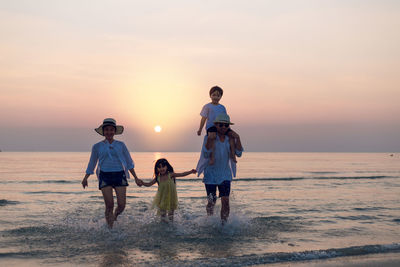 Full length of people on beach against sky during sunset