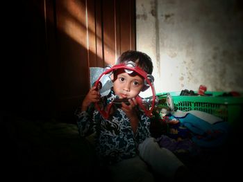 Portrait of boy holding musical equipment while sitting on bed at home