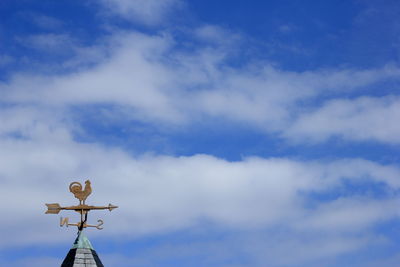 Low angle view of weather vane against cloudy sky