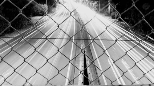 High angle view of light trails on two lane highway seen through chainlink fence