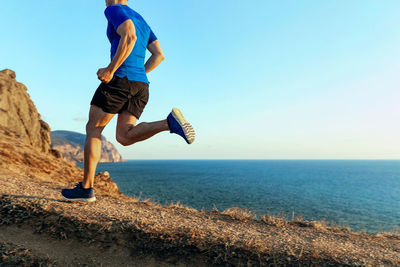 Athlete runner running mountain path in background sky and sea at sunset