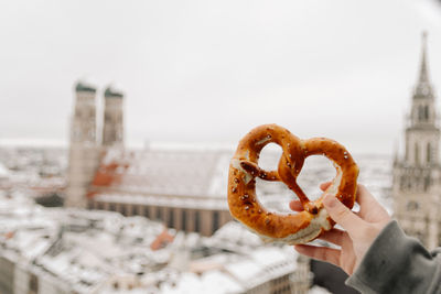 Close-up of hand holding pretzel against sky