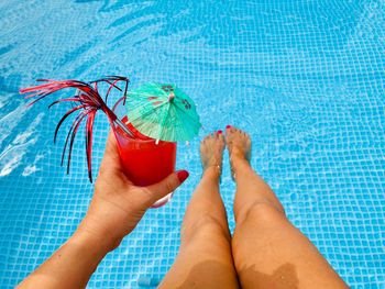 Low section of woman holding drink while sitting by swimming pool