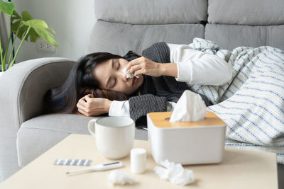 Woman blowing nose with tissue by lying on sofa at home