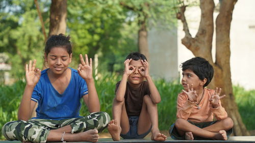 Two indian little girl and a boy doing meditate yoga asana on roll mat with eyes closed in park.