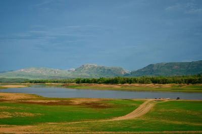 Scenic view of field by lake against sky