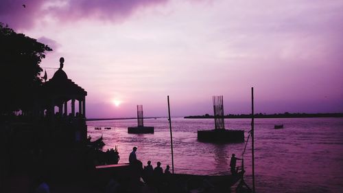 Silhouette wooden posts in sea against sky during sunset