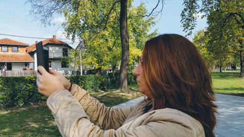 Side view of woman photographing from mobile phone at park