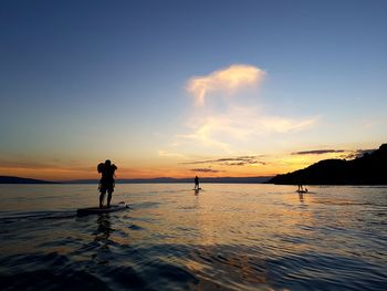 Silhouette people paddleboarding on lake against sky during sunset