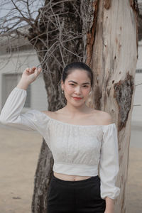 Portrait of smiling young woman standing by tree trunk