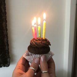 Cropped hands of woman holding cupcake with illuminated candles at home